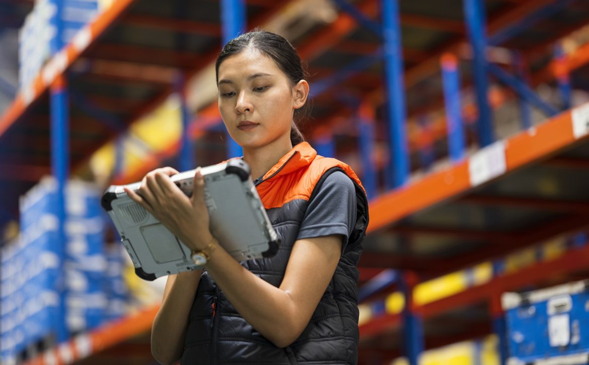 Improved Efficiency And Productivity with a Cloud Based WMS (Warehouse Management System). Low Angle View of a Warehouse Supervisor using industrial tablet to checking stock level and update by online inventory software in a large factory warehouse.