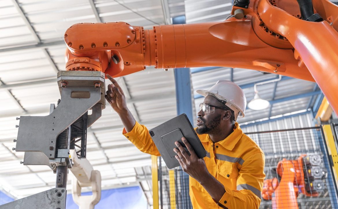 African engineer and tablet working with robotic arm at industrial manufacturing