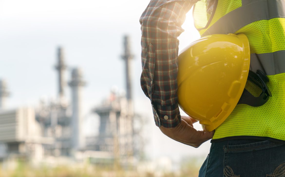engineering man with white safety helmet standing in front of oil refinery building structure in heavy petrochemical industry