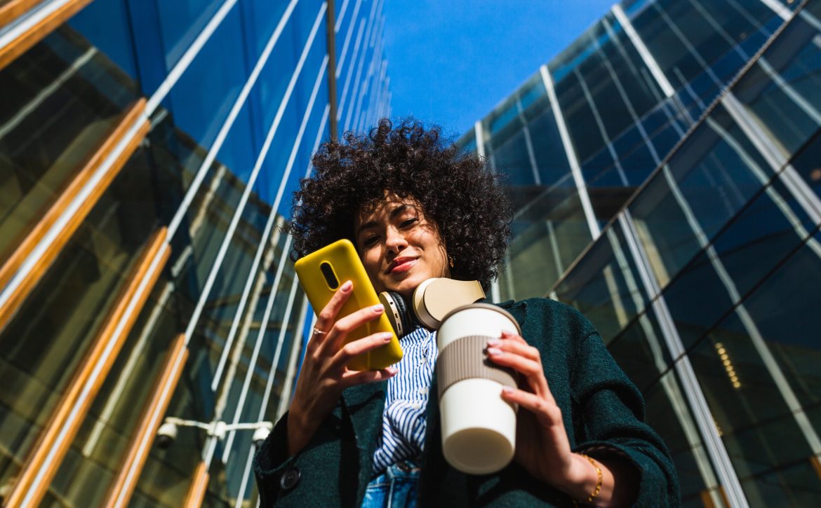 Low angle view of woman standing between commercial buildings using mobile phone.