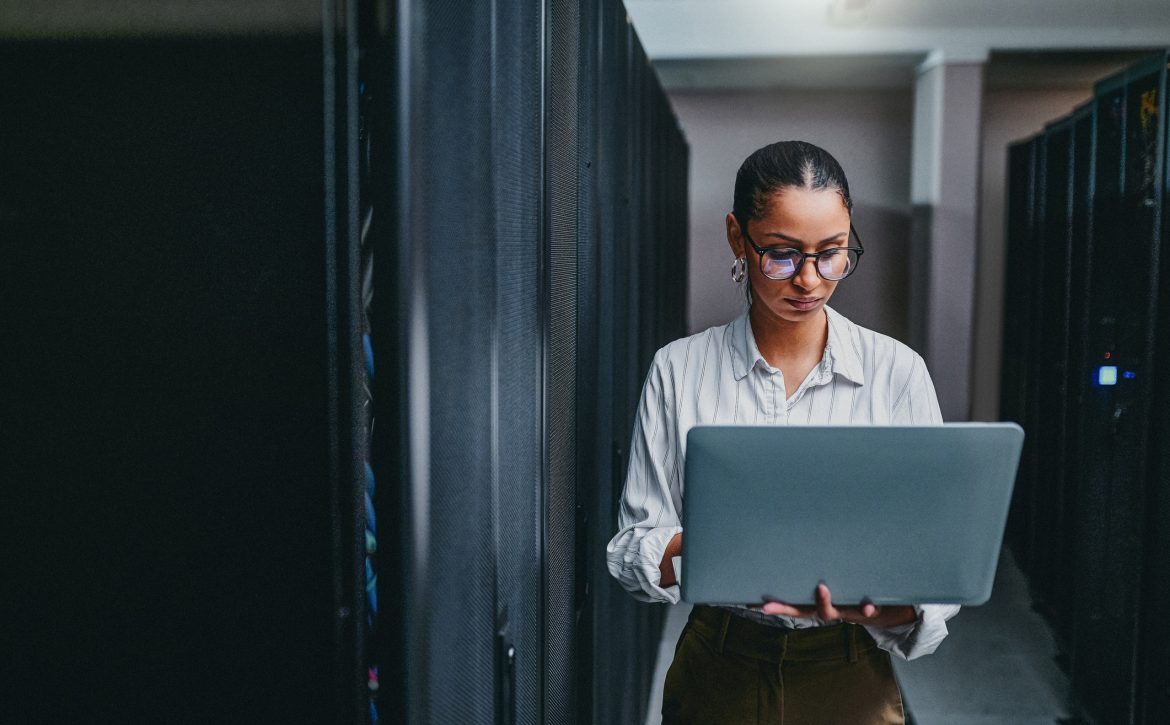 Shot of a young woman using a laptop while working in a server room